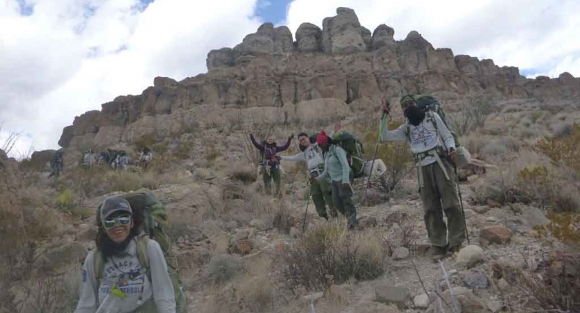 a group of gap year students descend from a rock formation in the desert on an outward bound semester expedition